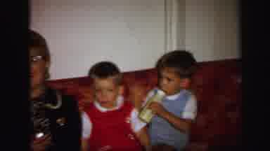 Lynbrook New York (1971): Toddler Wearing Blue Overalls Sits On Red Sofa Drinking