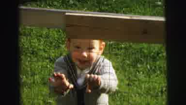 Lynbrook New York (1973): Baby Standing Behind A Cage And Holding Onto It Smiling