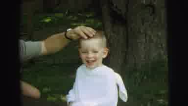 Lynbrook New York (1973): Man Wearing Green Shirt Rubs Head Of Boy Wearing White