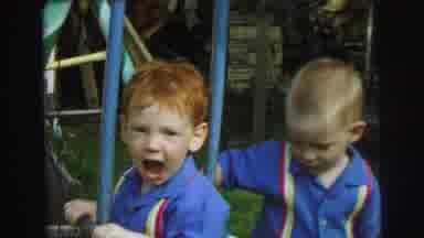 Lynbrook New York (1973): Boys Wearing Blue Shirts Ride On Green Swingset On A