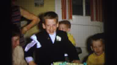 Lynbrook New York (1973): Boy Wearing Black Coat Looks At Cake While Woman Wraps