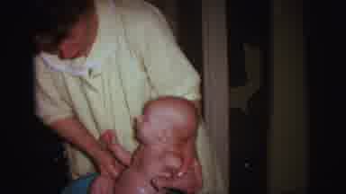 Lynbrook New York (1973): Woman Wearing Yellow Robe Bathes Baby In Blue Baby Tub