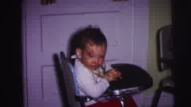 Lynbrook New York (1973): Baby Wearing White Shirt Sits In Blue High Chair With