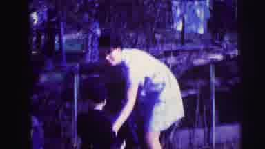 Lynbrook New York-1973: Woman Helps Young Boy With Red Bucket In Backyard