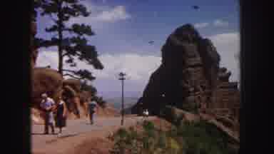 Denver Colorado (1958): People Walking Down An Asphalt Road Next To A Tall Rock At
