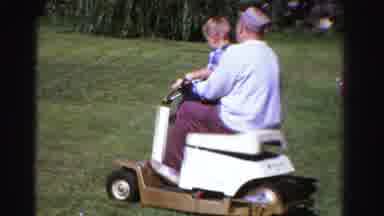 Ontario Canada (1958): Father And Son Riding On A Lawn Mower Together While Mother
