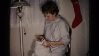 Hagerstown Maryland USA (1959): A Woman Seated On A Chair Opens A Present By A