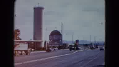 Nevada USA (1959): View Of Traffic Passing By Tan Tower Structure On A Sunny Day