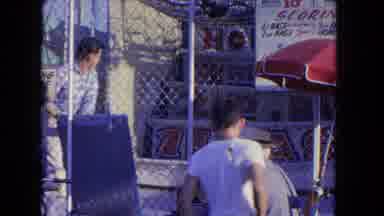 Los Angeles California USA (1962): People At A Carnival Hitting Baseballs Riding