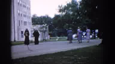 Illinois USA (1962): Women Walk Outside A Multiple Story Building On A Gravel Road