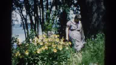Illinois USA (1962): An Older Woman Standing Amongst Green Bushes And Wild Flowers