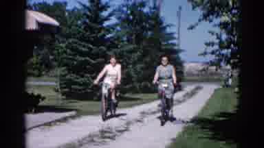 Illinois USA (1962): Two Young Women Riding Their Bikes On The Concrete Path In