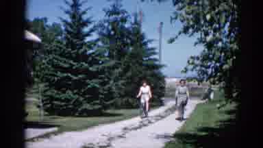 Illinois USA (1962): Two Women Bike Down A Dirt Road Side-By-Side In Dresses