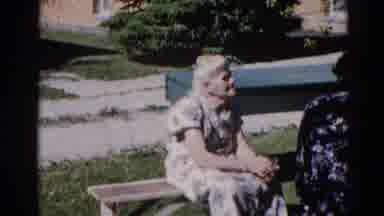 Illinois USA (1962): An Older Woman Wearing A White And Flowered Dress Sits On A