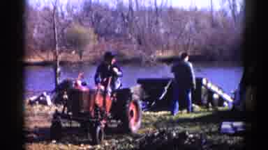 Illinois USA (1962): Two Men Using A Red Tractor To Pull Something From Lake On