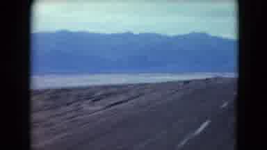 Nevada USA (1961): Driving On A Black Top Two Way Road With Mountains In