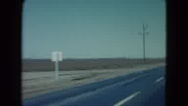 Nevada USA (1960): Driving Down A Blacktop Road Past Flat Farmland That Has Been