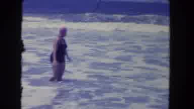 Los Angeles California USA (1962): Woman Wearing Black Swimwear Wades In Sea Surf
