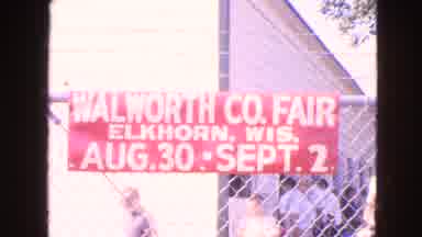 Walworth Wisconsin USA (1963): People Walking Along A Fence With A Sign About A
