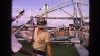 Walworth Wisconsin USA (1963): A Man In A Hat Walks Past People Riding On A