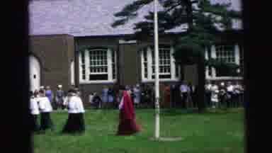 Camden New Jersey (1964): White And Red Cloaked Men Walk While Women Set Up
