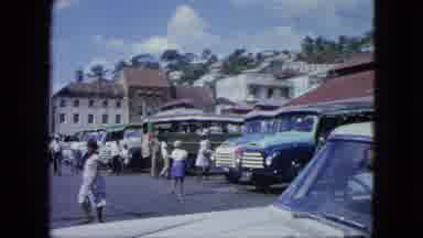 Grenada (1964): People Walking Through A Busy Parking Lot