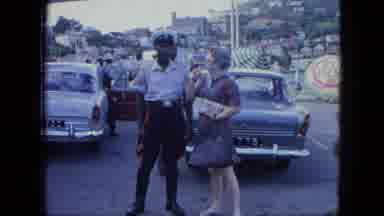 Grenada (1964): Black Police Officer Assists White Woman In Parking Lot Outside