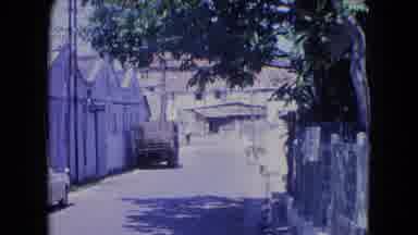 KINGSTON JAMAICA-1964: A Street With Buildings And Parked Vehicles Where Some Pedestrians Walk