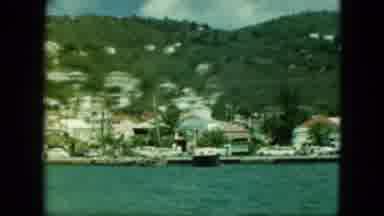 Saint Thomas (1964): Red And Blue Cars Drive Past Tan Building On A Sunny Day