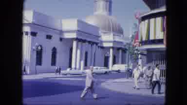 Venezula (1964): People Travel City Street By Large Building In Old Grainy Video