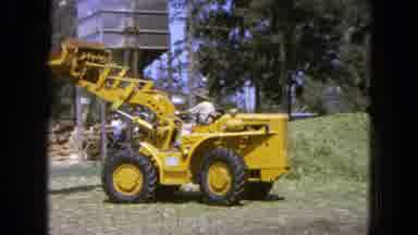 Pueblo Mexico (1965): Man Driving Yellow Digger Backward Catching Grass Then