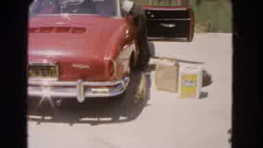 Barstow California USA (1966): Small Dog Runs Past Red Sports Car Towards Camera