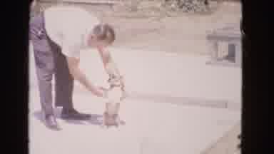 Barstow California USA (1966): Man Trying To Get Dog To Sit Up On Hind End With