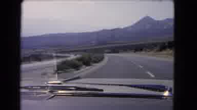 California USA (1966): Driving On The Highway Shows High Mountains Arising From