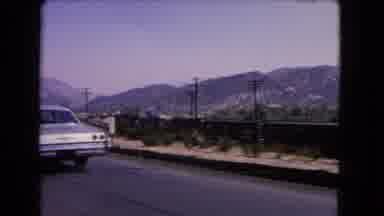 California USA (1966): Driving On Road Behind Blue Car With Big Mountain Range In