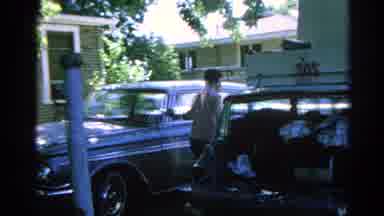 Danville Illinois (1966): Man Loads Items Into A Car While Family Sits On A Swing