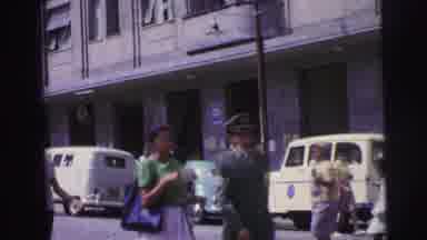 Brazil (1967): People Walk Adjacent To And Across An Urban Street With Parked Cars