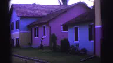 Brazil (1967): Person Walking Towards Colorful Homes Woman In Glasses Smiling By