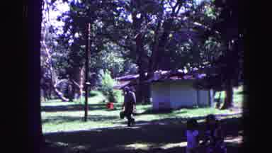 Galena Illinois USA (1967): A Holding Two Bags Walks Past Two Children Playing