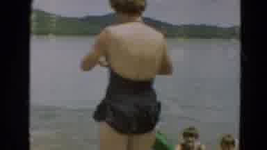 Minnesota US (1967): A Woman Looking At A Camera With Several Children Swimming In