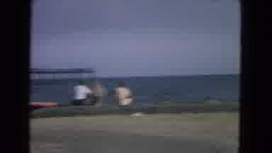 New Mexico USA (1967): Man In Shirt Sits On Beach While Two Boys Play In The Sea
