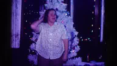 Minnesota USA (1968): Woman In Front Of Christmas Tree Tugs Shirt To Show How