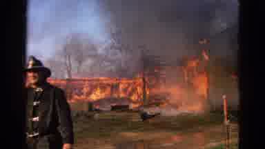 Wauconda Illinois USA (1968): Firefighter Walks Toward The Camera As A Large Barn