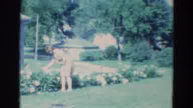 Diller Nebraska (1969): Barefoot Woman Admiring Flower Bed Near Corner Of House On