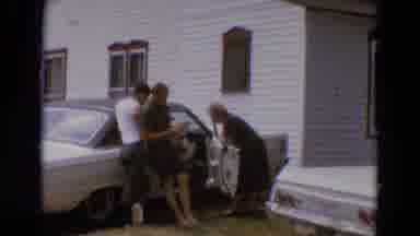 Diller Nebraska USA-1968: People Reading Newspaper Around A Car Outside Of A