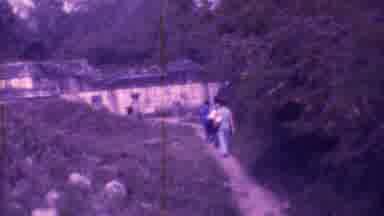 Mexico City (1973): Three People Walking Down A Dirt Path Toward A Building In The