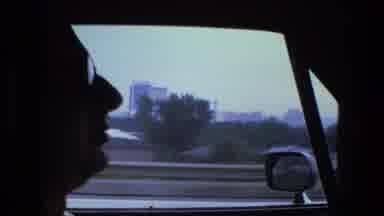 Fort Wayne Indiana (1974): Man Drives Vehicle On Road With Buildings And Hills In