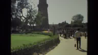 India (1974): People Walking In A Park With Green Grass And Trees With A Building