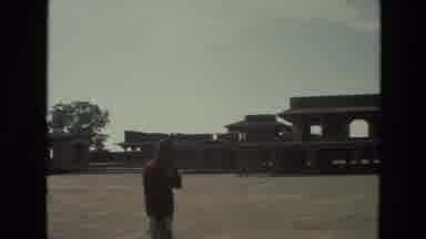 India (1974): Man Wearing Red Shirt Stands In Empty Parking Lot On A Sunny Day