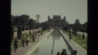 India (1974): People Walking Along A Reflecting Pool Outside Of A Large Building